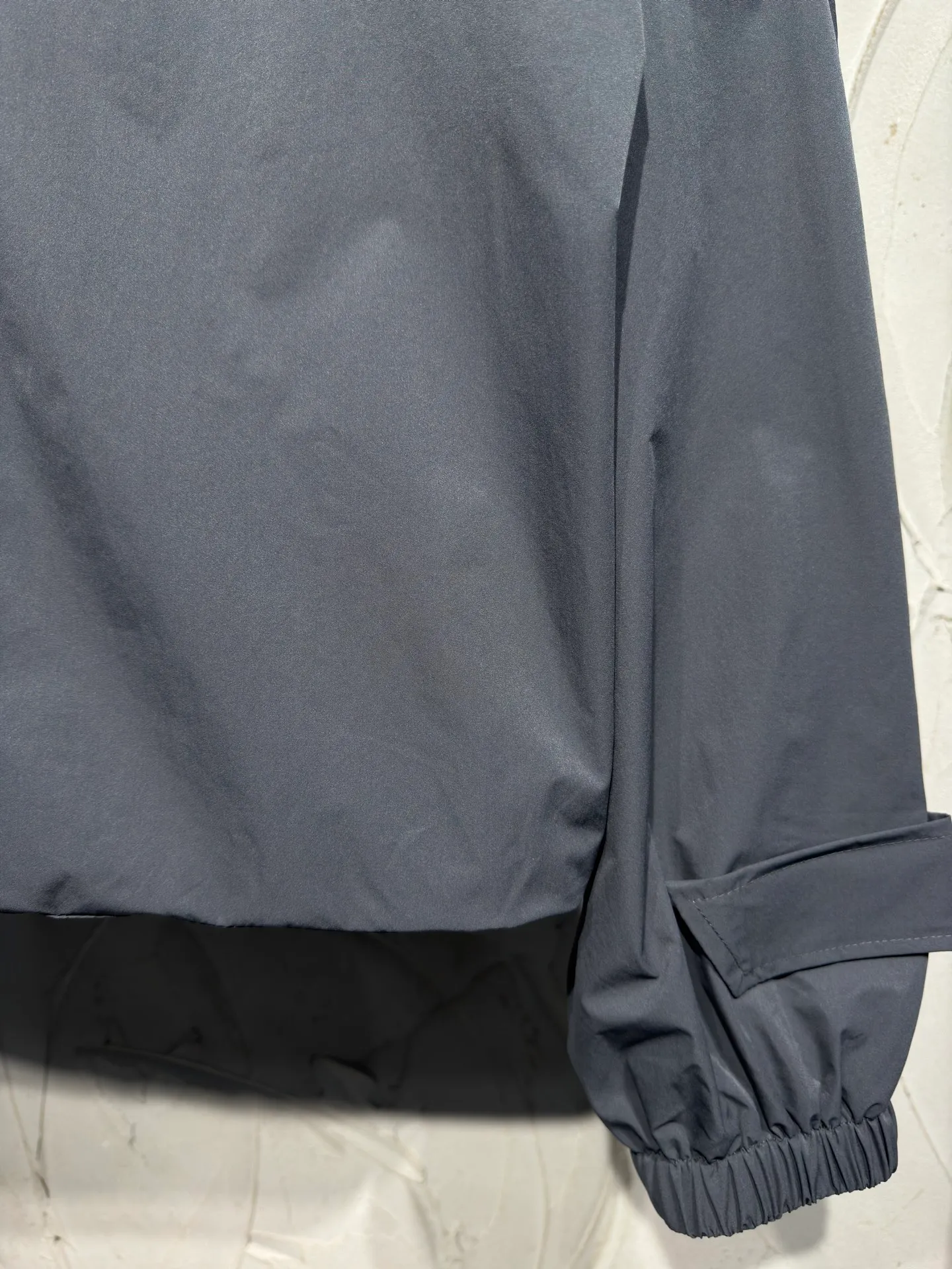 Acne Studios 26SS Large Lapel Short Jacket The fabric is made of 100% nylon (nylon/polyamide fiber) 75D high-density wrinkled nylon. The fabric has been permanently pressed and shaped by high temperature, and washed with high-pressure wrinkles at the factory to form its own irregular texture, permanently retaining the wrinkled texture, which will not disappear after washing. Matte matte coating removes the plastic glossy surface of nylon itself to create a low-key matte paper feel. Three-proof micro-coating, weak waterproof, anti-fouling, anti-static treatment, not easy to get dust. The interior is made of full-width mesh Breathable nylon lining, which reduces the stickiness of the nylon fabric to the body, improves air circulation, prevents sweating from sticking to the skin, and the zipper does not rub against the skin. The version adopts the raglan split topstitching process, and the front and rear panels are divided diagonally to expose even stitching. The three-dimensional dropped shoulders are loose and the fit is increased to increase the margin of movement. The back neckline is three-dimensional and high-density computer embroidered, and the embroidery lines are dense and not prickly. Customized all-metal matte nylon zipper, Genuine Leather embossed brand letters on the zipper leather tab, zipper tape with same color nylon fit to the body, double-locked reinforcement on both sides of the zipper to prevent pulling and tearing. Color: Gray Size: S M L